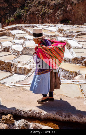 Einheimische peruanische Ureinwohner auf Salineras de Maras / Maras Salzbergwerk. Salzgewinnung in Maras Salinen, Terrassen und Teichen im Heiligen Tal von Peru. Stockfoto