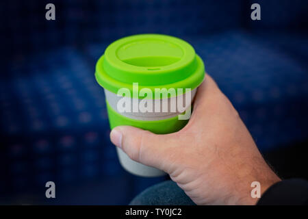 Ein Mann hält eine wiederverwendbare Kaffeetasse, während auf einem Zug saß. Stockfoto