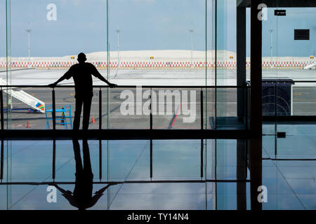 Denpasar, Bali, Indonesien: 05.Juni 2019 - Mann durch Glasfenster am Flughafen, als er für seinen Flug wartet. Stockfoto