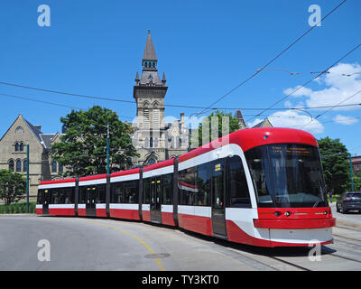 TORONTO - JUNI 2019: Eine lange Gelenktriebwagen biegt, wie es um die Kurve vor der gotischen Stil Gebäude an der Universität von Toronto geht weiter Stockfoto