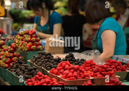 Arbeitnehmer zeigen verschiedene bunte Beeren auf dem Tisch zum Verkauf an der Granville Public Market, Vancouver, British Columbia, Kanada. Stockfoto