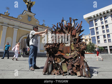 Ein Mann nimmt ein Bild von der Eiserne Thron, während der Präsentation auf dem Platz der Unabhängigkeit in Kiew, Ukraine. Die 600 kg Kunst Arbeiten von Armee freiwillige Denis Bushtets berechtigt "Eiserne Thron des Ostens' ist der Tank Stücke, Patrone, Gürtel, Fragmente von Raketen, Maschinengewehre, Granaten, Soldat, Flakons und andere militärische Artefakte, die auf der vorderen Linie mit Russland aufgenommen wurden - unterstützte Separatisten im Osten der Ukraine. Ein Prototyp eines berühmten Bügeleisen Thron von Spiel der Throne TV-Serie ist eine Erinnerung an einen blutigen Konflikt, der bereits seit 2014 etwa 13.000 Menschen getötet hat. Stockfoto