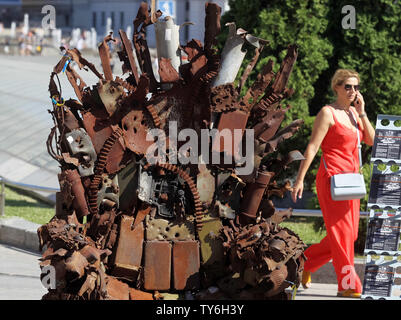 Eine Frau geht neben den Eisernen Thron, während der Präsentation auf dem Platz der Unabhängigkeit in Kiew, Ukraine. Die 600 kg Kunst Arbeiten von Armee freiwillige Denis Bushtets berechtigt "Eiserne Thron des Ostens' ist der Tank Stücke, Patrone, Gürtel, Fragmente von Raketen, Maschinengewehre, Granaten, Soldat, Flakons und andere militärische Artefakte, die auf der vorderen Linie mit Russland aufgenommen wurden - unterstützte Separatisten im Osten der Ukraine. Ein Prototyp eines berühmten Bügeleisen Thron von Spiel der Throne TV-Serie ist eine Erinnerung an einen blutigen Konflikt, der bereits seit 2014 etwa 13.000 Menschen getötet hat. Stockfoto