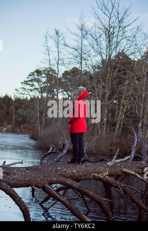 Person trägt einen roten Mantel stehen auf einer Brücke gemacht Von einem Schnittbaum mit einem Fluss im Hintergrund Stockfoto