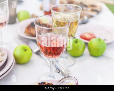 Gegrillte Zackenbarsch, Brille mit weißen und rosa Wein, Teller, Gemüse, Salat und Obst auf den Tisch. Sommerfest im Hinterhof. Horizontale Schuß Stockfoto