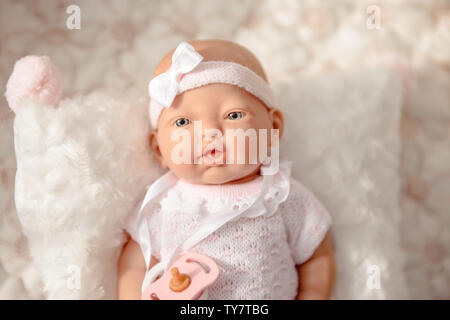 Baby Doll in weißen hellen Kleidung auf beigen Hintergrund isoliert. Stockfoto