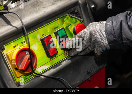 Ein männlicher Arbeiter in Arbeitshandschuhe drückt den roten Knopf auf die Maschinensteuertafel in der Werkstatt oder Fabrik. Die Industrie und die Produktion im Maschinenbau. Stockfoto