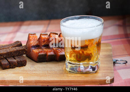Ein Glas helles Bier mit geräuchertem Fisch und Schwarz gebratenes Brot mit Knoblauch. Bier und Bier Snack auf einem Holzbrett close-up. Stockfoto