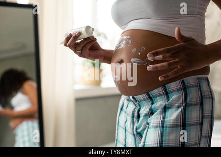 Hände einer schwangeren Frau, die Ihre creaming Bauch. Stockfoto