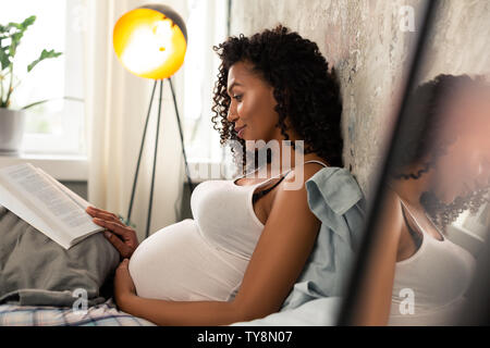 Die werdende Mutter mit einem Buch auf ihrem Bett. Stockfoto