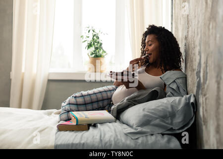 Schwangere Frau cookies Essen in ihrem Bett. Stockfoto