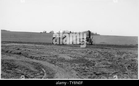 Mechanisierte Straße - Einstufung in die Besoldungsgruppe. Des Lacs NWR, North Dakota; Umfang und Inhalt: Eine kleine Planierraupe Ziehen einer Reiten in eine riesige Fläche von offenen Felder pflügen, mit landwirtschaftlichen Gebäuden und Kulturen im Hintergrund. Stockfoto
