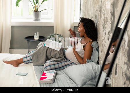 Schwangere Frau essen, sich mit Büchern. Stockfoto