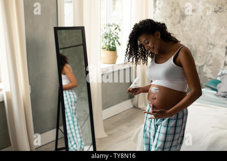 Schwangere Frau kümmert sich um ihren Bauch Haut. Stockfoto