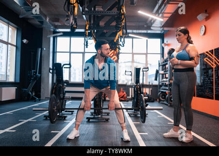 Dunkelhaarige Trainer anheben Barbell es an seinen Kunden Stockfoto