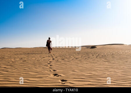 Junge selbstbewusste Frau alleine auf Wüste Sand unter den Dünen an einem heißen sonnigen Tag mit blauen Himmel Stockfoto