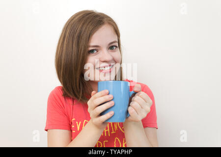 Portrait von lächelnden jungen kaukasischen Frau Mädchen mit einem Becher Kaffee mit beiden Händen, als ob sagen: Guten Morgen! Stockfoto