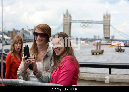 Touristen ein Bild mit der Tower Bridge mit der Olympischen Ringe in die reflektierende Glas von einem französischen TV-Studio am Ufer der Themse in London am 21. Juli 2012 gebauten geschmückt. Die letzten Vorbereitungen werden mit Eröffnungsfeier für die Olympischen Spiele 2012 sechs Tage entfernt. UPI/Terry Schmitt Stockfoto