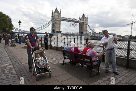 Touristen genießen gutes Wetter am Ufer der Themse mit der Tower Bridge mit der Olympischen Ringe in London am 21. Juli 2012 geschmückt. Die letzten Vorbereitungen werden mit Eröffnungsfeier für die Olympischen Spiele 2012 sechs Tage entfernt. UPI/Terry Schmitt Stockfoto