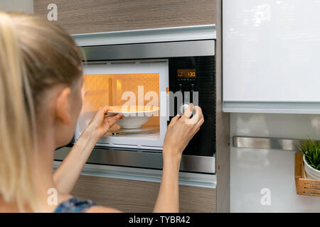 Frau warm, das Essen in der Mikrowelle zu Hause Stockfoto