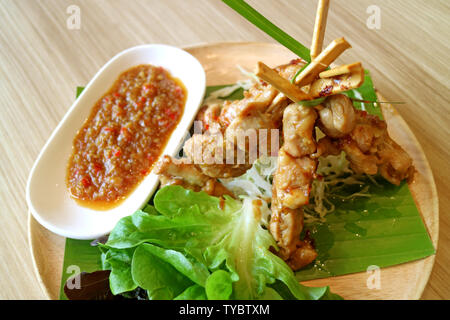 Gegrilltes Hähnchen mit pikanter Sauce und grünem Salat serviert auf Holzplatte Stockfoto