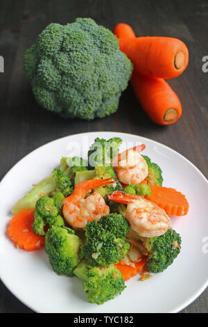 Gesundes Gericht von Rühren gebratene Garnelen mit Broccoli und Karotten auf weiße Platte serviert. Stockfoto