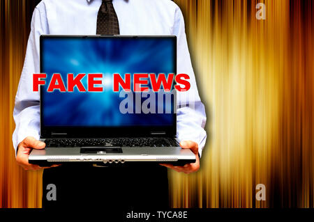 Mann hält einen Laptop mit Worten gefälschte Nachrichten auf dem Bildschirm Stockfoto