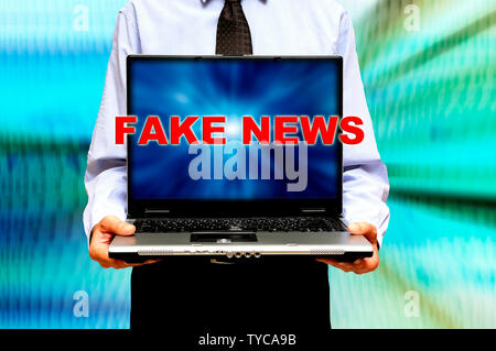 Mann hält einen Laptop mit Worten gefälschte Nachrichten auf dem Bildschirm Stockfoto
