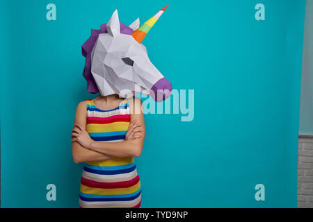 Junge, kreative Mädchen, dass auf Head 3D weißes Einhorn Kopf, auf blauem Hintergrund im Studio posieren. Schlankes, elegantes Modell in gestreiften Kleid mit gekreuzten Händen. Stockfoto