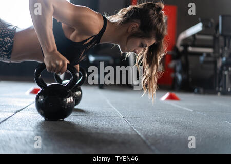 Sportliche Frau, Push-ups in der Turnhalle mit Kettlebells Stockfoto