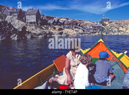 Historisches Archivbild von Britisch 1980s Mutter & Kinder auf Mediterrane Familienpaket Urlaub Reise in bunten maltesischen Fischerboot An verlassenen Holzfilm-Drehgebäude aus dem 1980 Popeye Filmen Sie, wie wir im Anchor Bay Village waren 80s Malta Stockfoto