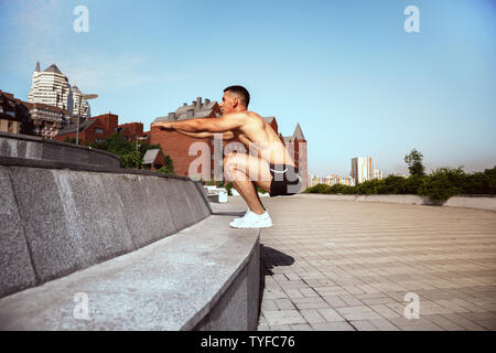 Ein muskulöser männlichen Athleten, Training im Park. Gymnastik, Training, Fitness Workout Flexibilität. Sommer Stadt im sonnigen Tag auf Hintergrund Feld. Aktiven und gesunden Lebensstil, Jugend, Bodybuilding. Stockfoto