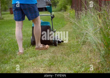 Der Mann mäht den Rasen mit dem Benzin Rasenmäher im warmen Sommer Stockfoto