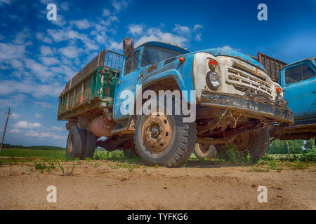 Alten rostigen LKW oder Lkw im Freien in einem Feld geparkt neben einem zweiten Fahrzeug gesehen her Boden bis auf eine blaue bewölkter Himmel Stockfoto