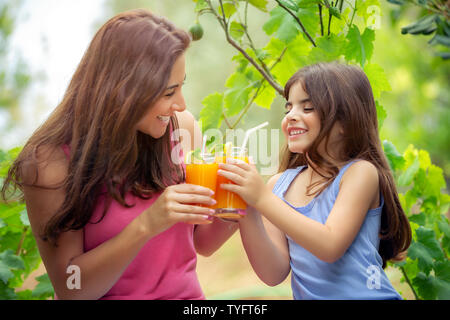 Portrait Of Happy fröhliche Familie trinken Orangensaft auf dem Picknick im Garten in sonniger Tag, Mutter und Tochter mit frischen Getränken, schönen Sommer Stockfoto