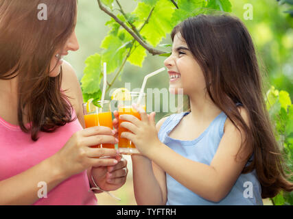 Portrait Of Happy fröhliche Familie trinken Orangensaft auf dem Picknick im Garten an einem sonnigen Tag, Mutter und Tochter in ein gesundes Getränk, glücklich Stockfoto