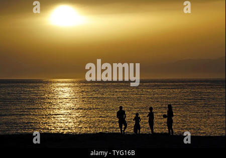 Silhouette einer Familie bei Sonnenuntergang an der Küste in Matala, Kreta Stockfoto