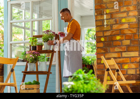 Lächelnd Mann stand in der Nähe der Blume ad acta zu legen, und Spritzen von Pflanzen. Stockfoto