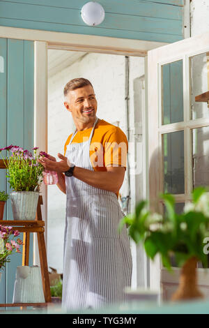 Blumenhändler in eine gestreifte Schürze besprühen die Pflanzen draußen. Stockfoto