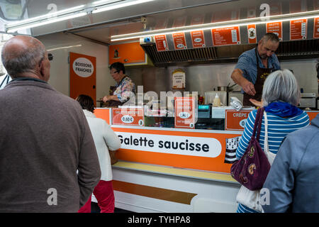 Die Menschen in der Warteschlange für Galette saucisse (gegrillte Würstchen in Krepp umwickelt) im Donnerstag Wochenmarkt in Dinan, Bretagne, Frankreich Stockfoto
