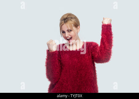 Portrait von glücklich erfolgreiche Freude schöne junge blonde Frau in Rot Bluse stehen und ihren Sieg feiern mit überraschten erstaunt. ind Stockfoto