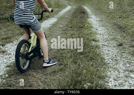 Mädchen in gestreiften Kleid Reiten Fahrrad. Die Zeit im Freien. Kinder spielen draußen im Frühjahr, im Sommer. Kindheitserinnerungen. Wandern im Park, Wald. Das Gehen auf Reise, Abenteuer in der Wildnis Stockfoto