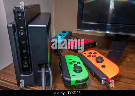 Spiel vier Controller mit unterschiedlichen Farben, neben einem Nintendo Switch auf einem hölzernen Tisch Konsole. Stockfoto