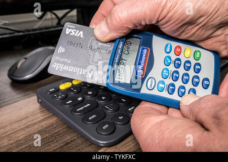 Man Hände mit bundesweiten Bank Card Reader und Visa Debit Card, mit 'Karte' auf dem Display, neben Computer Tastatur, für on-line-Transaktion. Stockfoto