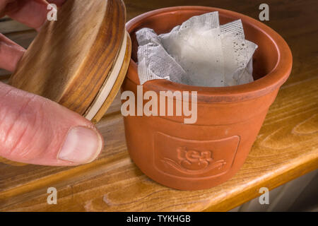 Nahaufnahme eines Menschen Hand ersetzt den Deckel aus einer luftdichten terracotta Ton storage Topf, nachdem Sie es mit Teebeutel. Stockfoto