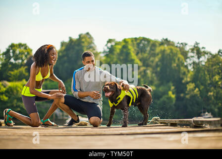 Glückliches junges Paar spielen mit ihrem Hund auf einem Steg. Stockfoto