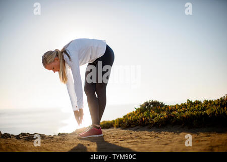 Junge Frau nimmt einen Bruch von ihrer Joggen entlang der Klippen in der Sunrise Licht zu dehnen. Stockfoto