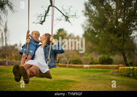 Mutter und Tochter schwingen auf ein hölzernes Schwingen. Stockfoto