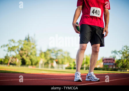 Älterer Mann hält ein Diskus auf einem Sportplatz. Stockfoto