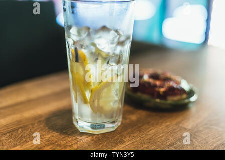 Kalte Limonade mit Eis und Zitronen in ein hohes Glas mit einem Einweg-röhrchen. Schokolade Donut mit Ankleideraum. Lecker und ungesunde Frühstück. Stockfoto